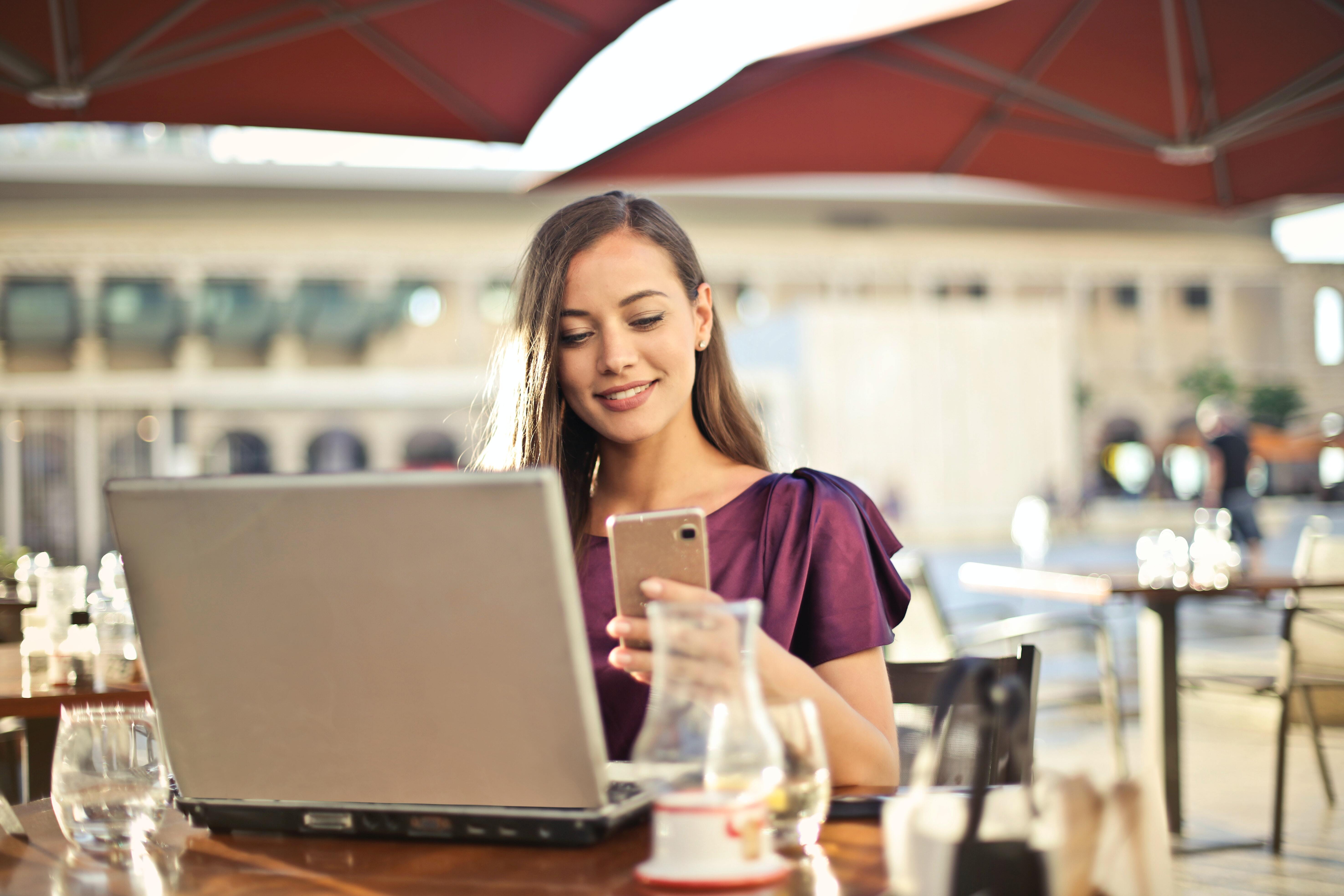 image of a woman checking her phone with her laptop in front of her